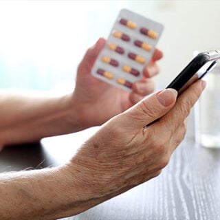 A picture of a mesothelioma patient's hand holding a smartphone to use an app to track his medications he holds in his other hand.