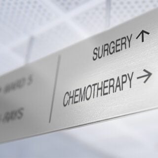 A ceiling sign in a hospital hallway points one direction for chemotherapy and another direction for surgery, symbolizing the quandary posed by the study covered in this post.