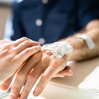 Image shows a close-up shot of an oncology nurse's hands placing tape on a patient's intravenous infusion line. The line resembles those used for immunotherapy treatments.