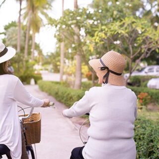 A mesothelioma patient and her friend are wearing sun hats and recreationally riding beach cruiser bicycles together.