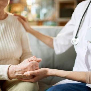 Doctor and mesothelioma patient holding hands while discussing palliative care.