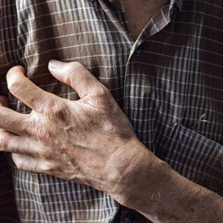 Image depicts an older person clutching a hand over their chest, which illustrates some of the heart-related side effects of immunotherapy drugs.