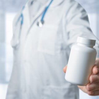A doctor wearing a white coat with a blue stethoscope draped around the collar holds out a bottle of orphan drug pills.